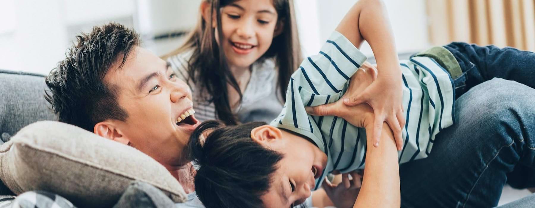 father plays on a couch with his young children